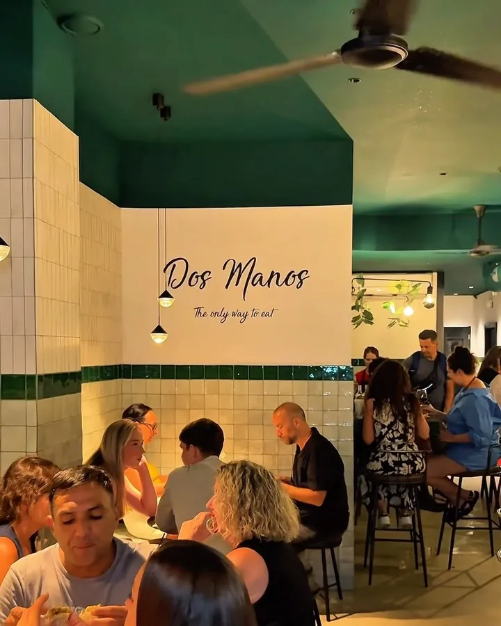 Interior de DosManos con azulejos blancos y verdes, y el rótulo «Dos Manos, the only way to eat» en la pared