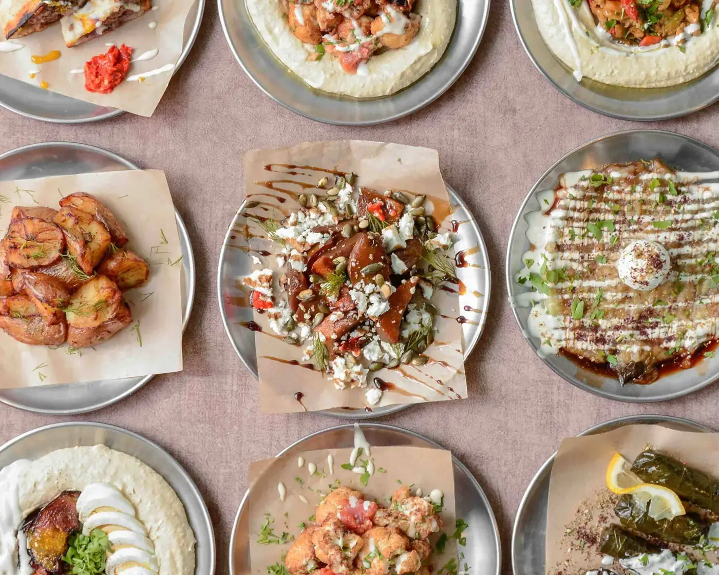 Mesa vista desde arriba con platos de DosManos: hummus, boniato, coliflor, berenjena y pitas
